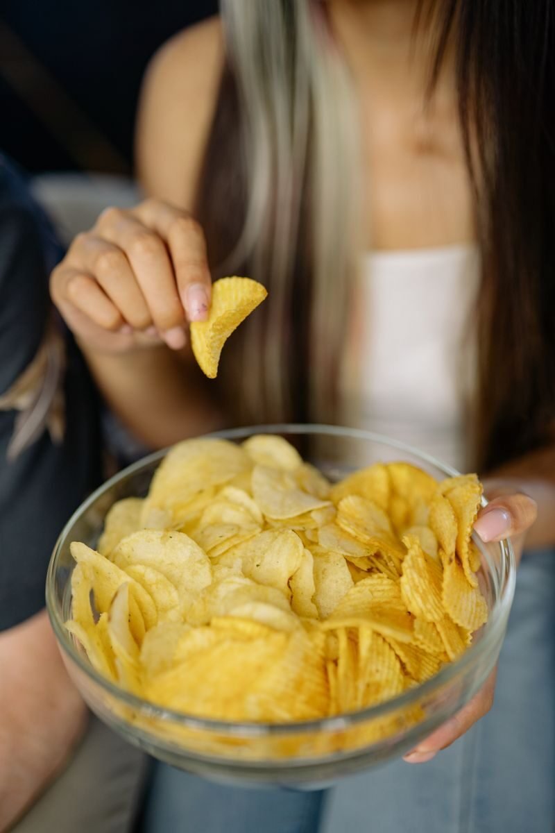Young woman enjoying a bowl of crispy potato chips, highlighting snack time delight.